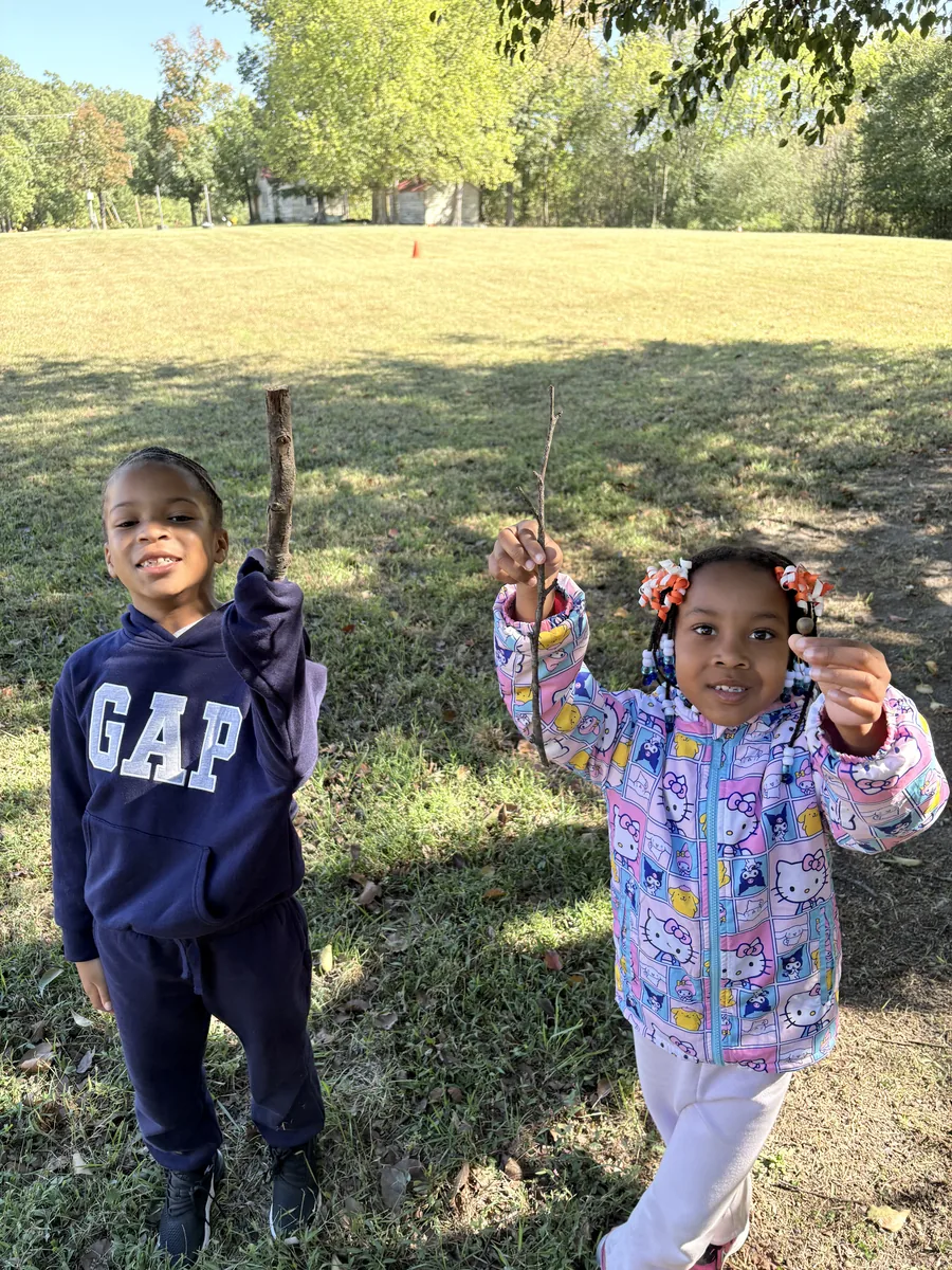 Two Laurel students holding up sticks they found outside on the campus field