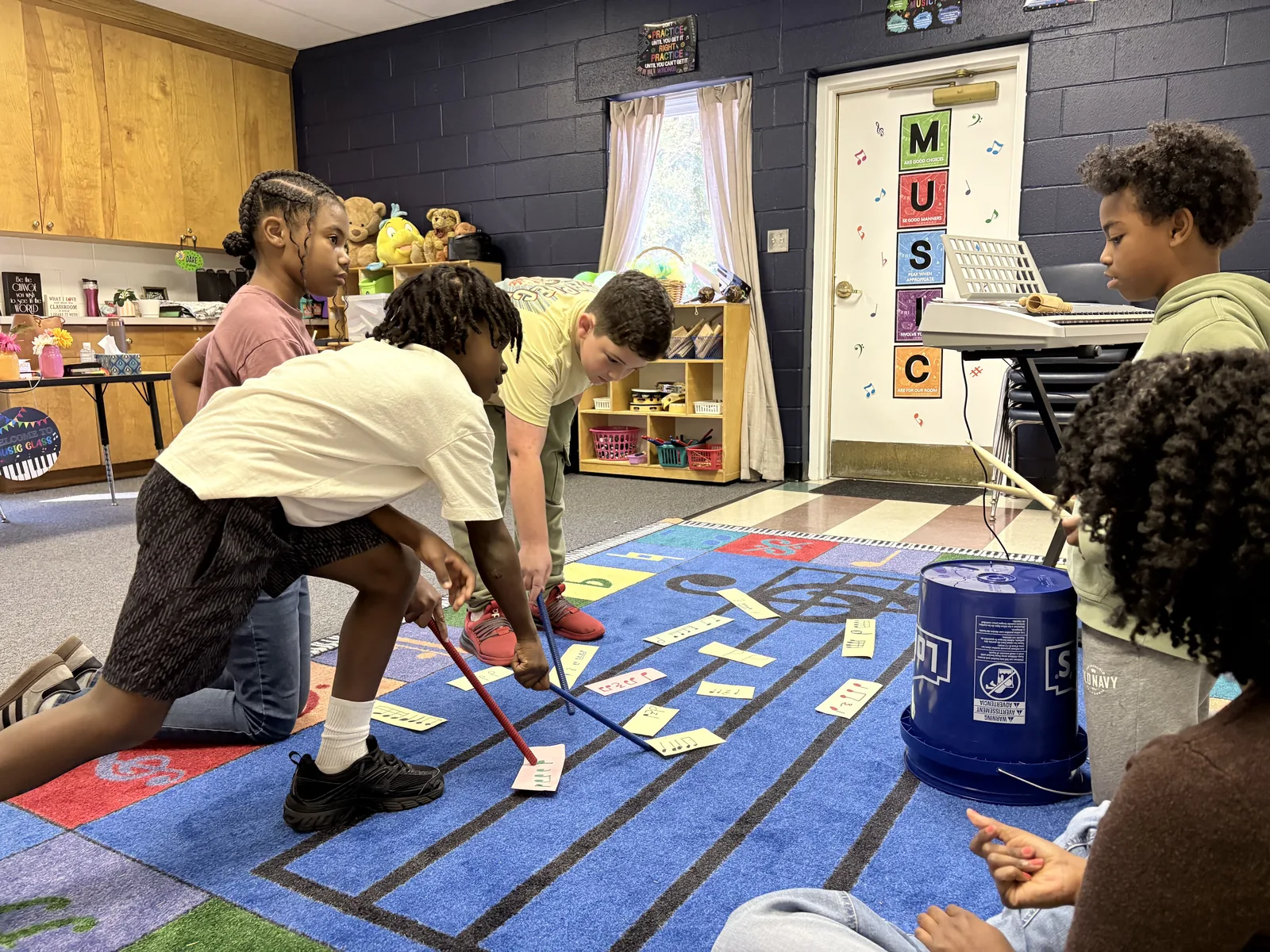 Laurel students placing rhythm cards on a floor-sized music staff rug during music class
