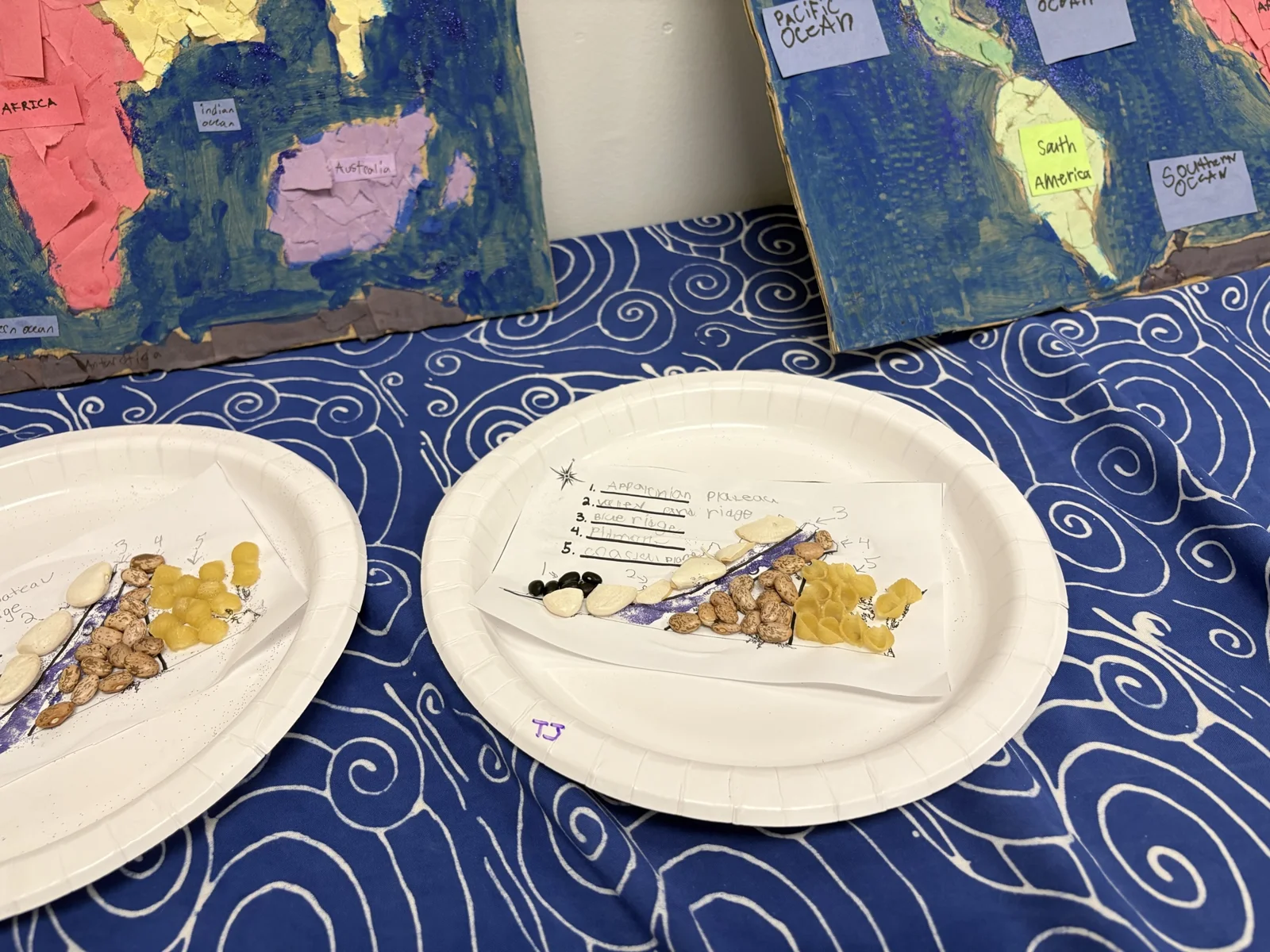 Student map projects made on paper plates alongside painted canvases