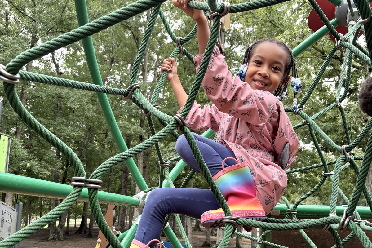 A young Laurel student climbing high on the rope dome in the Play Forest